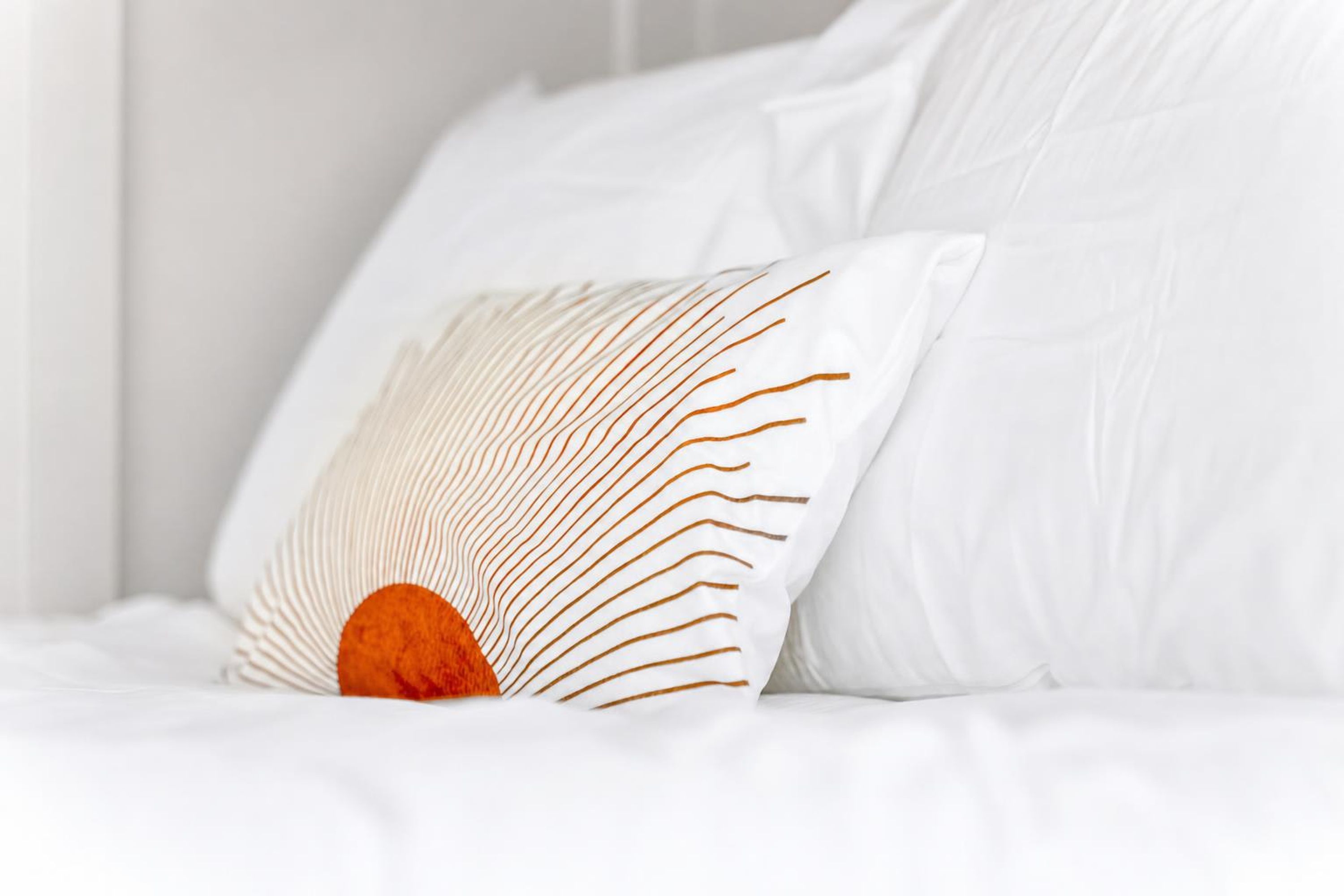 A white bed with a pillow featuring a geometric pattern.