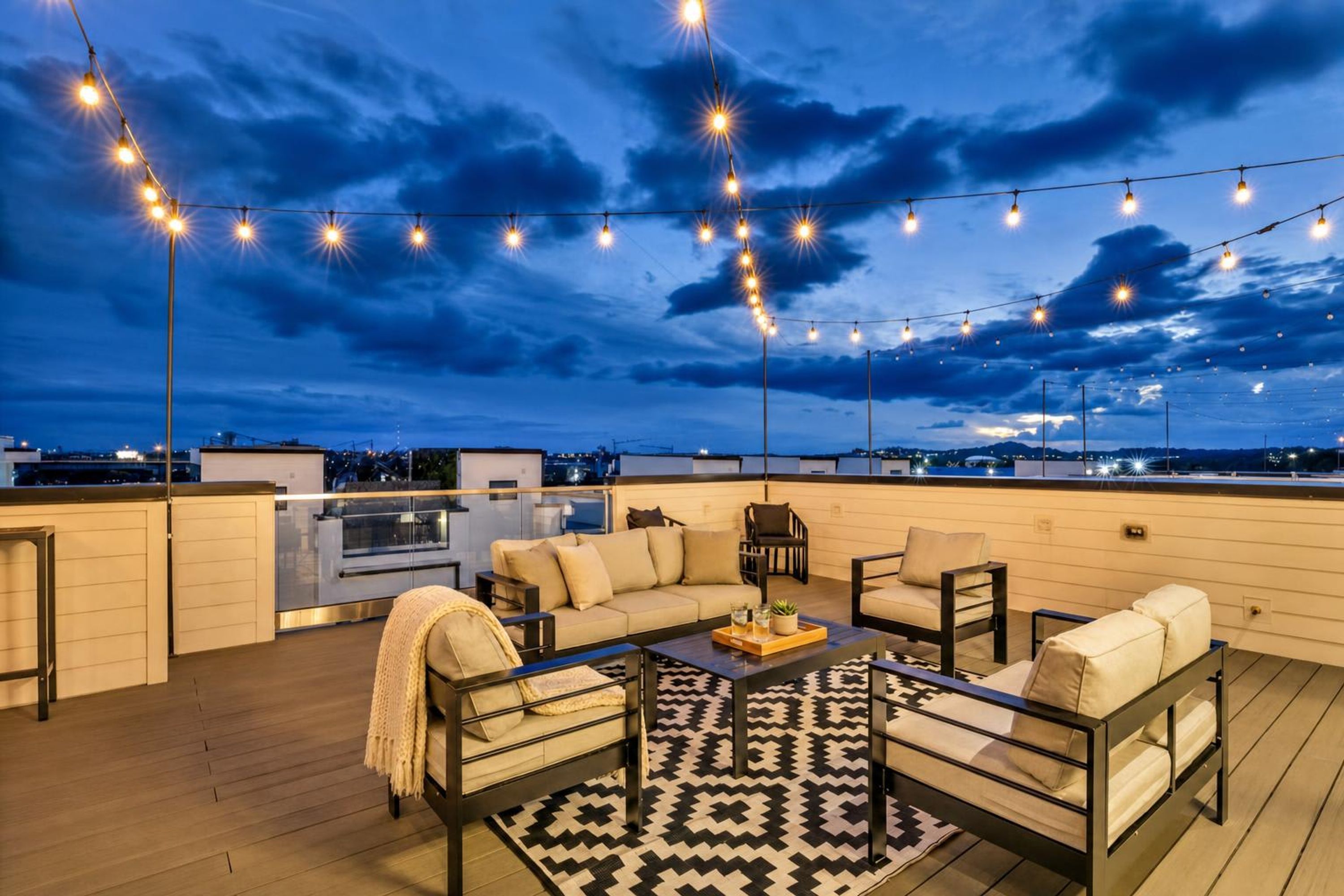 A rooftop terrace with outdoor seating, string lights, and a view of the cityscape.