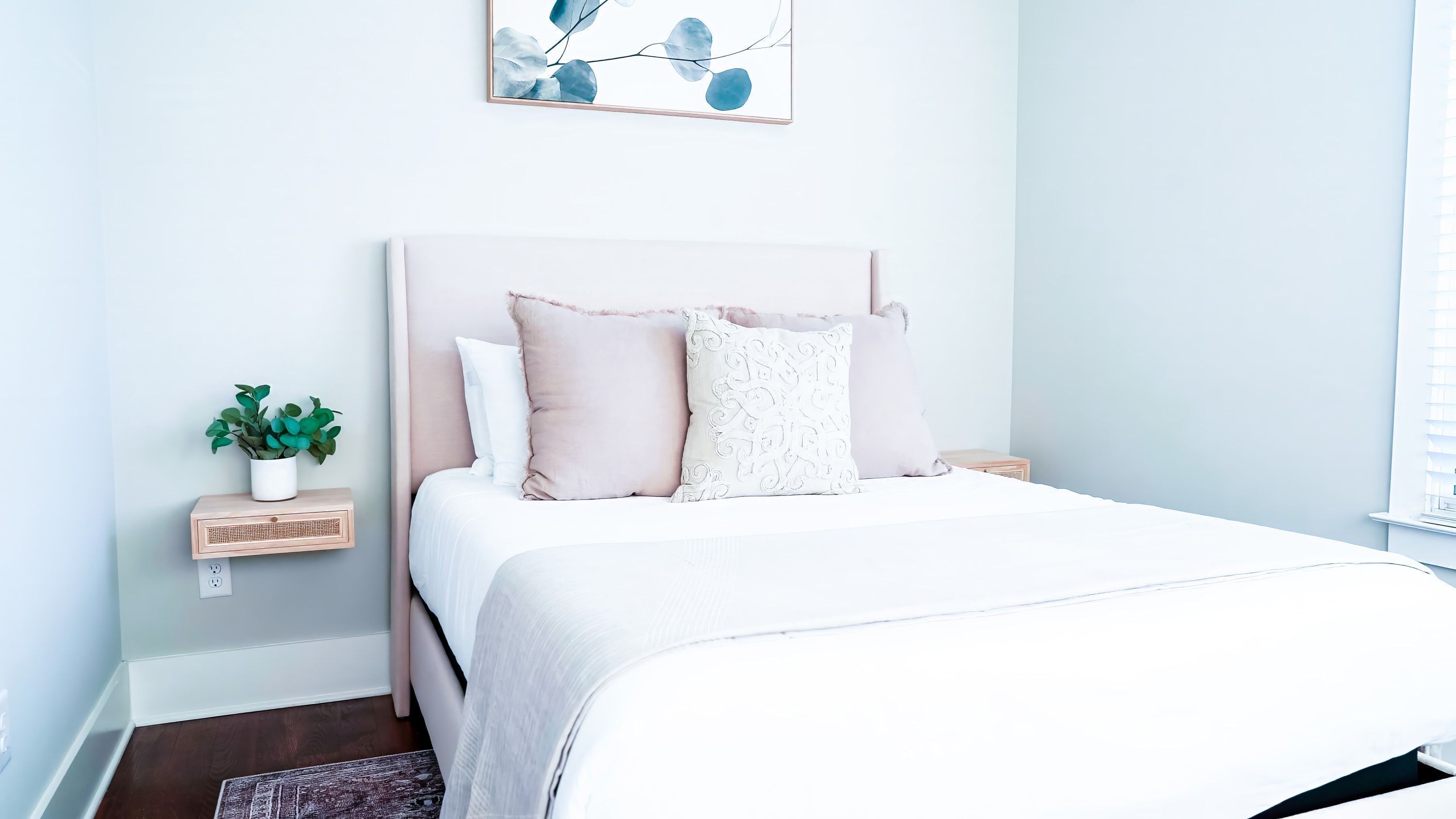 A neatly arranged bedroom with a bed, a bedside table with a plant, and a wall-mounted artwork.