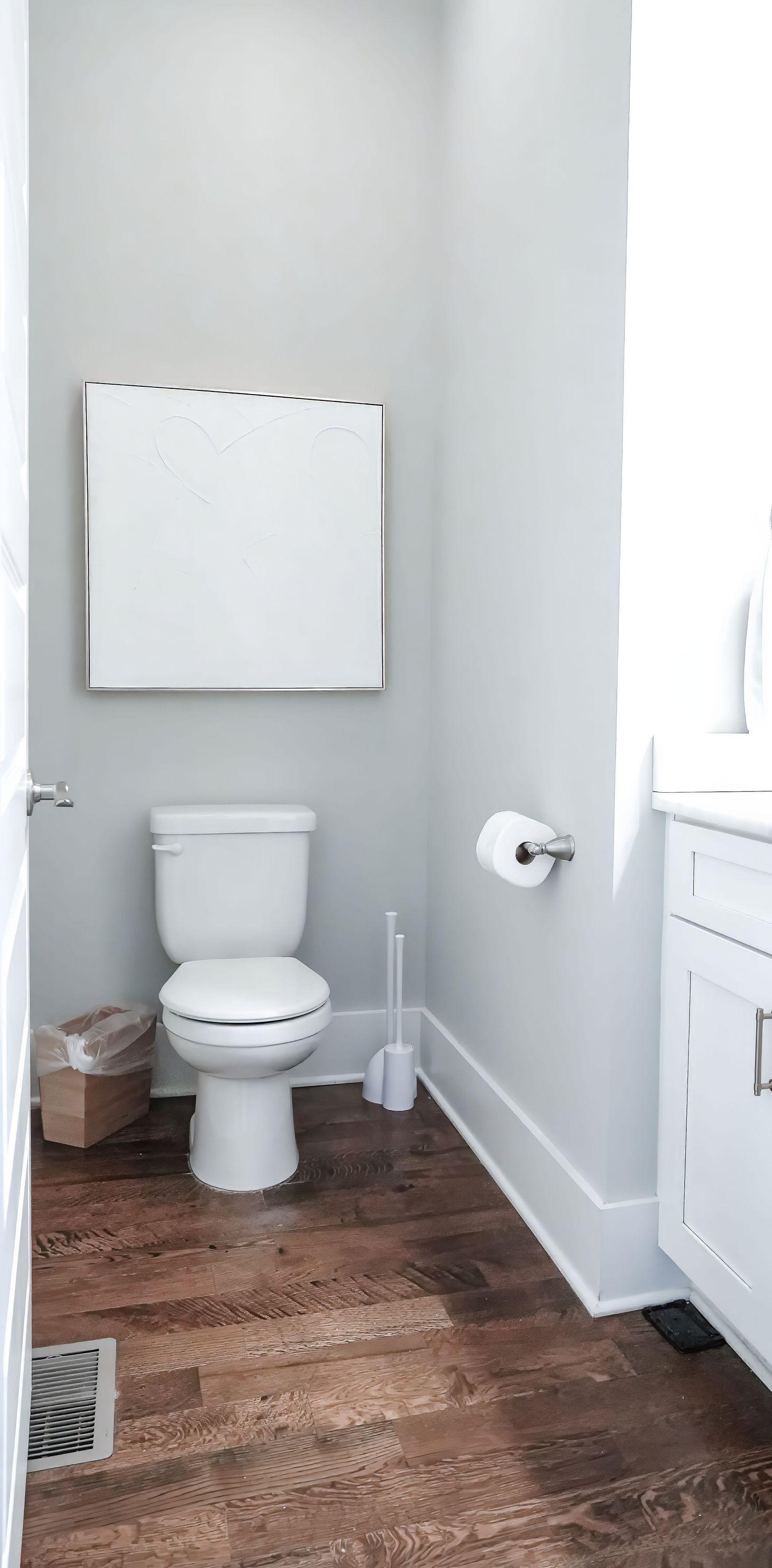 A bathroom with a white toilet, a wooden floor, and a white cabinet.