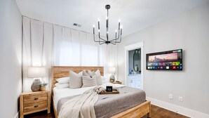 A modern bedroom with a wooden bed, bedside tables, a chandelier, and a mounted TV displaying a cityscape. - City Views Pool Hot Tub Mini Golf (Nashville)
