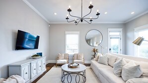 A modern living room with a white sofa, a round coffee table, and a television mounted on the wall. - City Views Pool Hot Tub Mini Golf (Nashville)