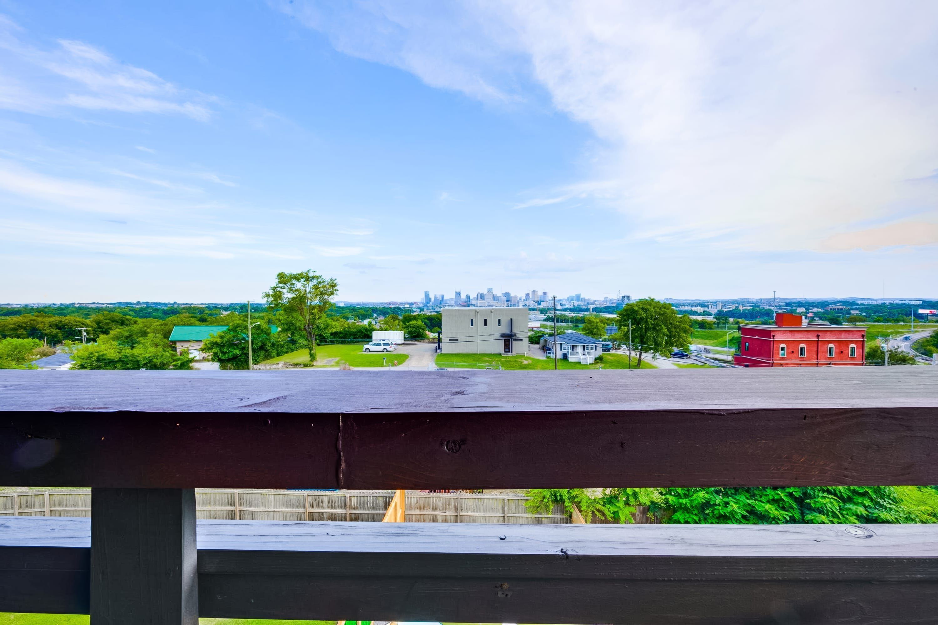 A view from a balcony overlooking a cityscape with a prominent building in the distance, a red building, and a green field in the foreground.