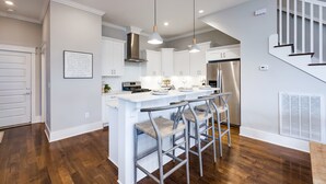 A modern kitchen with white cabinets, a stainless steel range hood, and a central island with bar stools. - City Views Pool Hot Tub Mini Golf (Nashville)