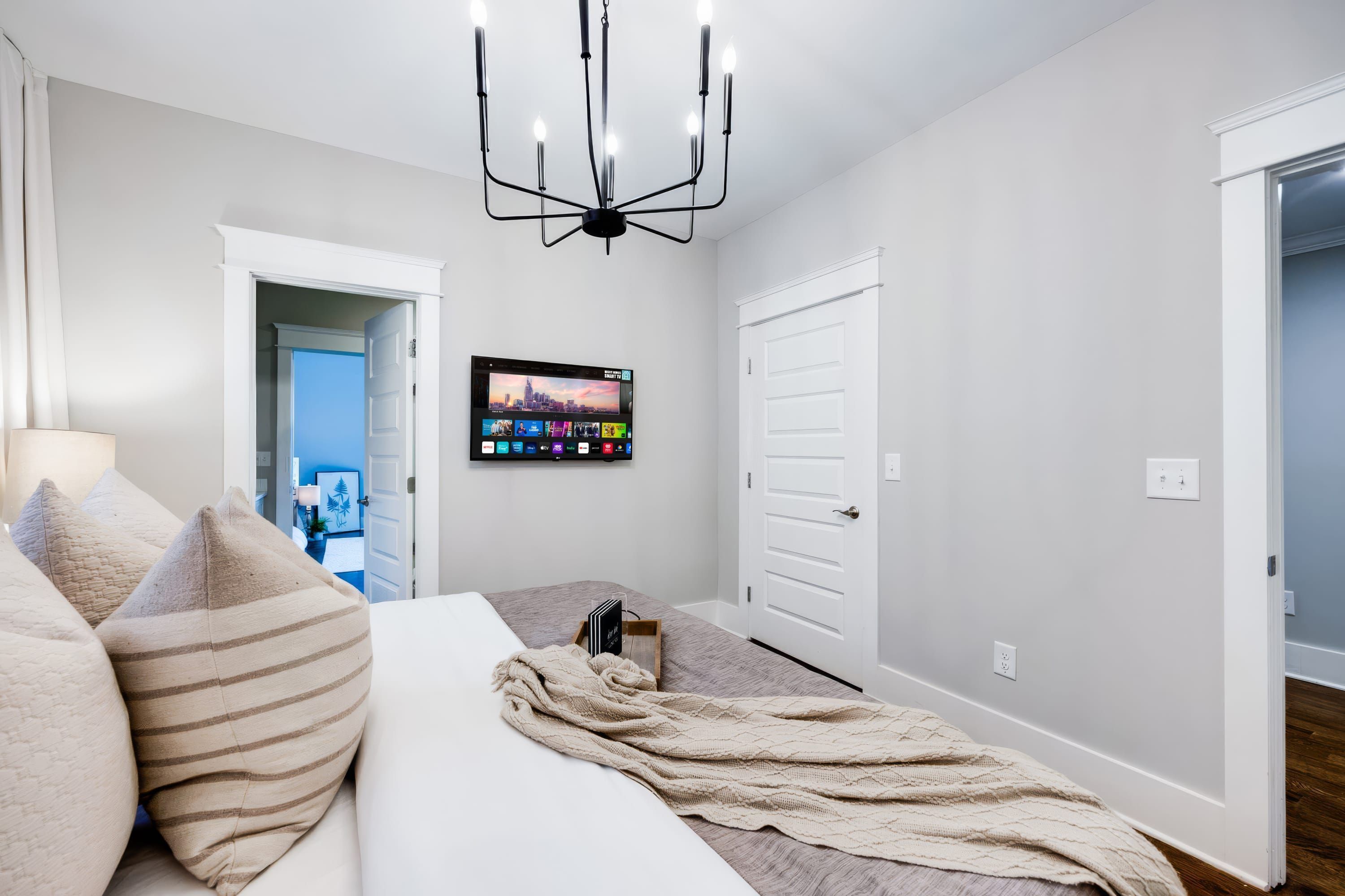 Un dormitorio con cama, televisión montada en la pared y una puerta que da a otra habitación.
