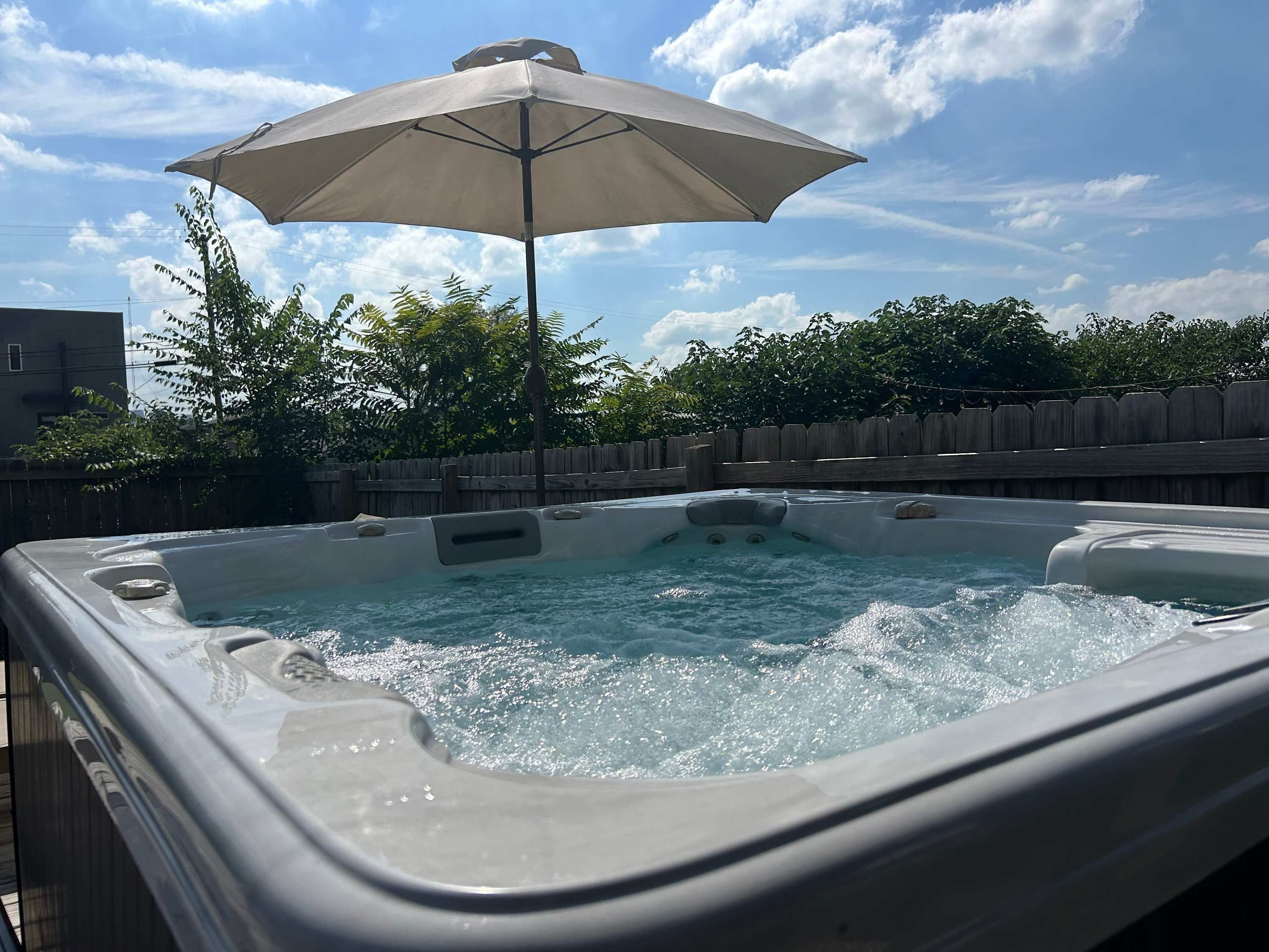 A hot tub with a wooden fence and an umbrella in the background.
