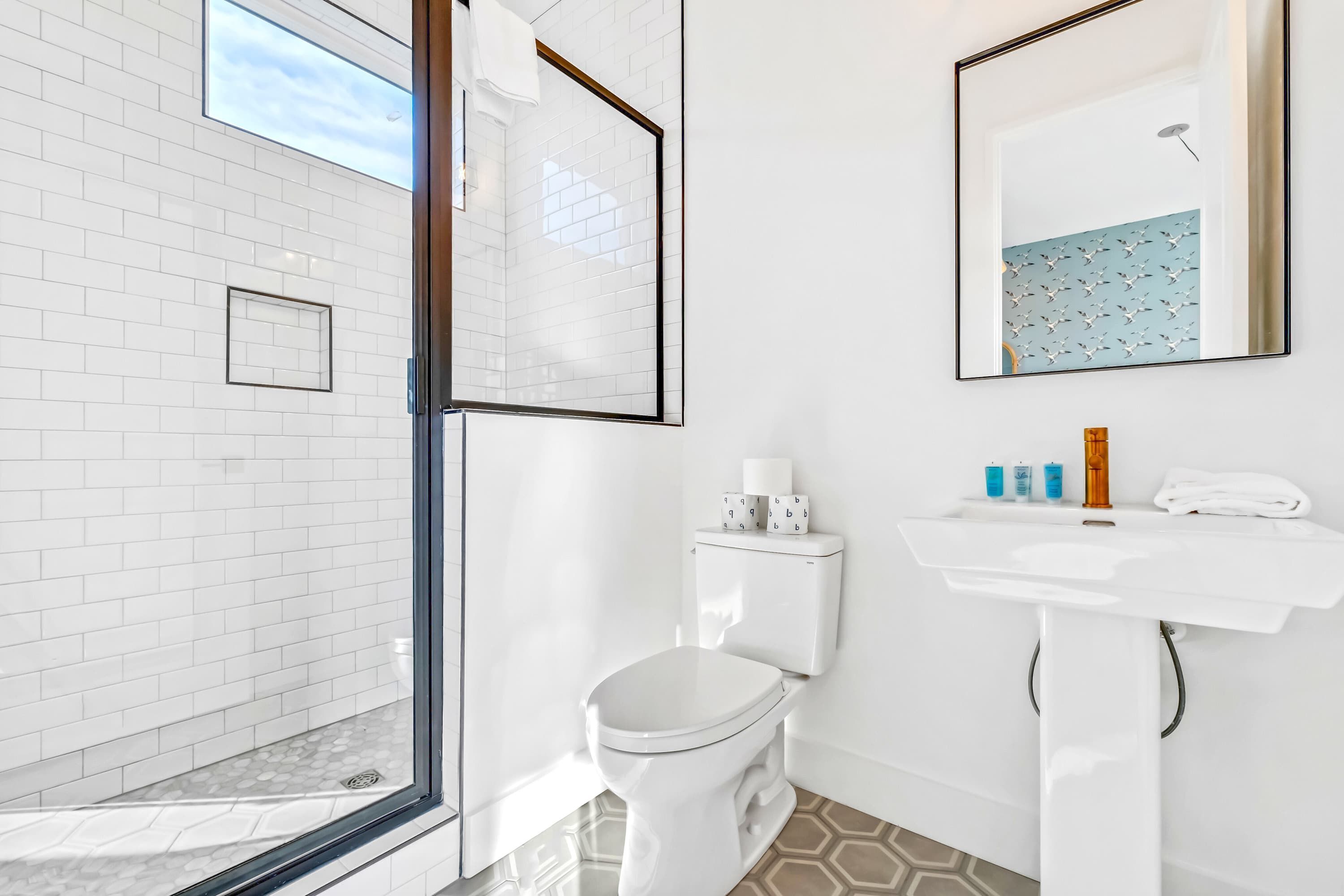 A modern bathroom with a white toilet, a sink with toiletries, and a shower area.