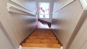 Eine Holztreppe mit weißer Wandverkleidung und Blick in einen Raum mit Fenster und Blumen.