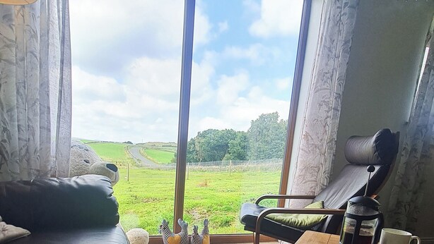 Ein Wohnzimmer mit großem Fenster, einem Ledersofa, einem Couchtisch und einem Sessel.