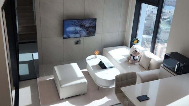 Een moderne woonkamer met een flatscreen televisie aan de muur, een bank, een salontafel en een eethoek met een tafel en stoelen.