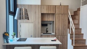 Een moderne keuken met een centraal eiland, twee barkrukken, een inbouwoven en een trap.