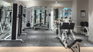 Een fitnessruimte met diverse trainingsapparaten, waaronder krachttoestellen en losse gewichten, in een ruime ruimte met een gepolijste vloer en spiegelwanden.