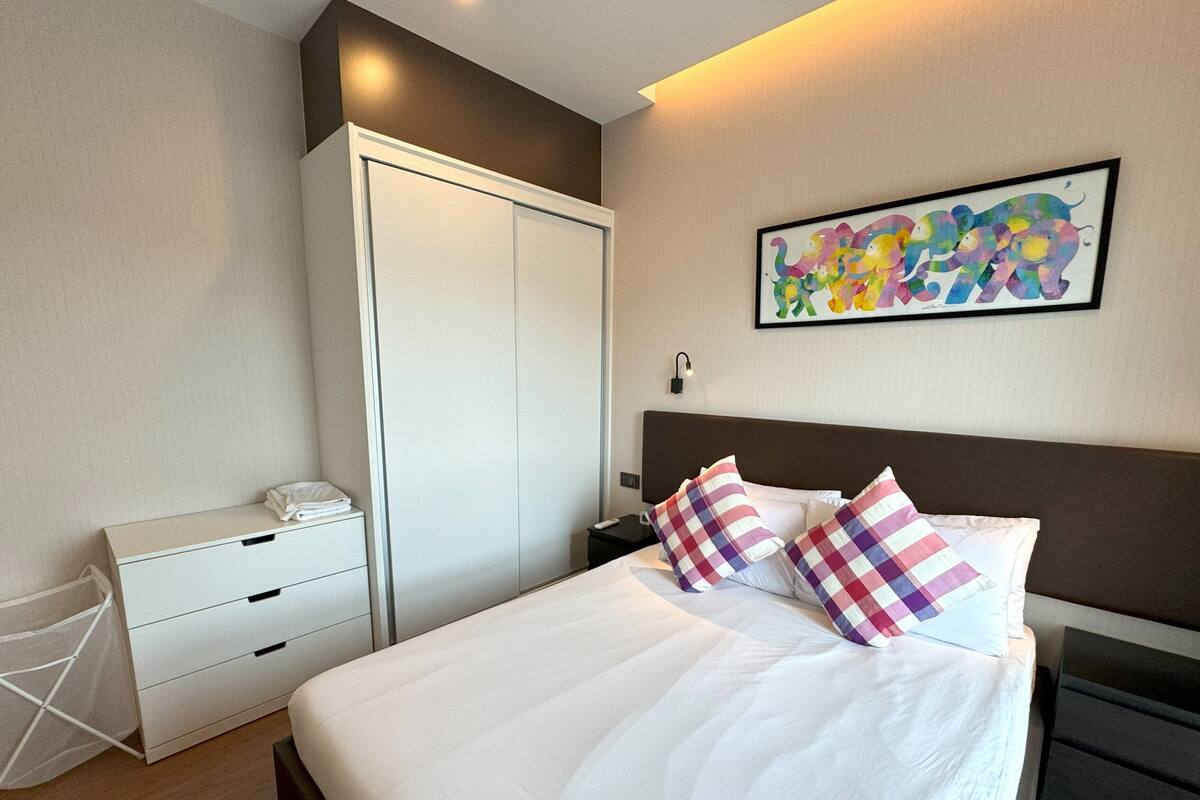 A neatly arranged bedroom with a bed, a wardrobe, a bedside table, and a wall-mounted artwork.
