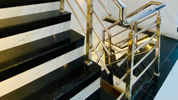 Un escalier moderne avec des marches en marbre noir et blanc et des rampes en acier inoxydable.
