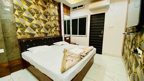 Una habitación de hotel con cama, ventana, equipo de aire acondicionado y una pared con diseño geométrico.