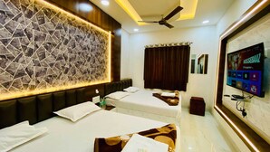 Une chambre d’hôtel avec deux lits, un décor mural moderne, un ventilateur de plafond et un téléviseur diffusant une émission.