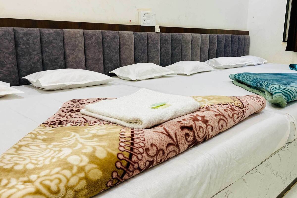 Un letto rifatto con cuscini bianchi e fantasia, un asciugamano piegato e una coperta a righe blu e verdi.