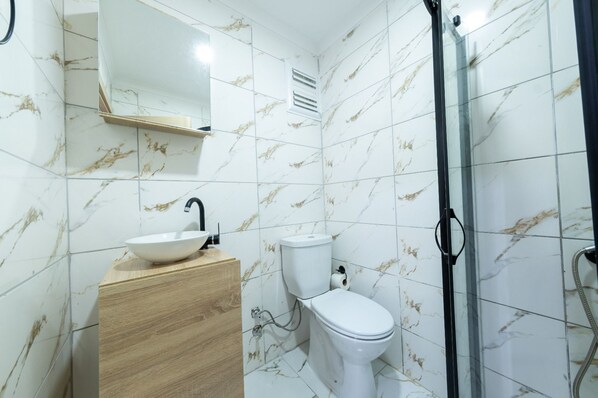 A bathroom with a marble backsplash, a wooden vanity, a white sink, a toilet, and a glass shower enclosure. - Luxery Kral Hotel Beşiktaş (Istanbul)