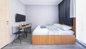 Ein modernes Schlafzimmer mit einem Holzbett, einem Schreibtisch mit Stuhl, einem Flachbildfernseher und einem großen Fenster mit Vorhängen.