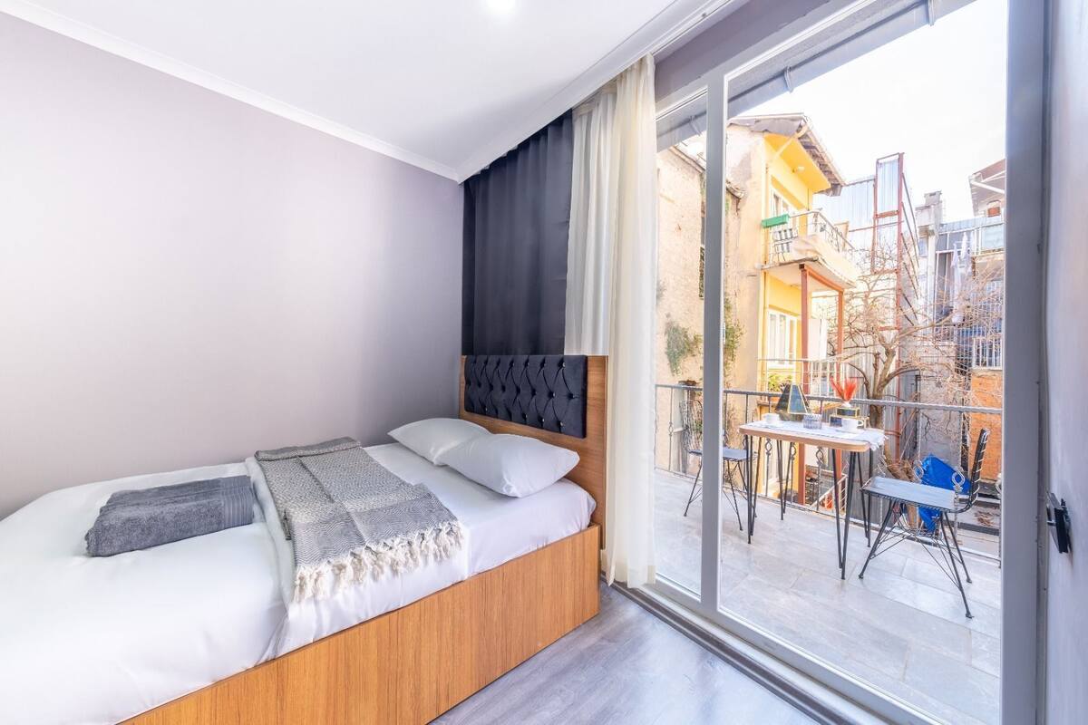 Ein Schlafzimmer mit Bett, Fenster und Blick auf einen Balkon.