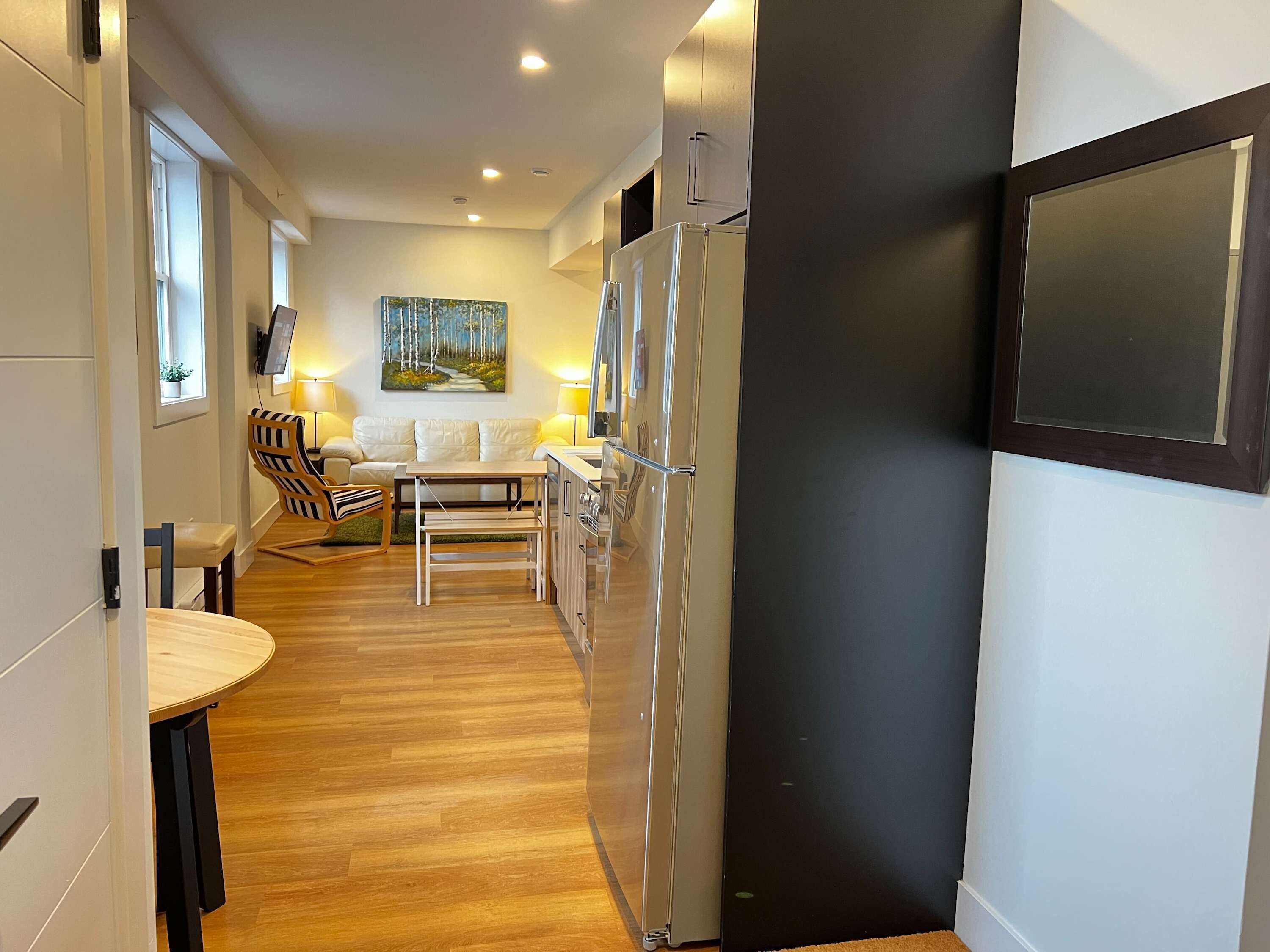 Une cuisine moderne équipée d’un réfrigérateur, un coin repas avec une table et des chaises, et un salon avec un canapé et un tableau.