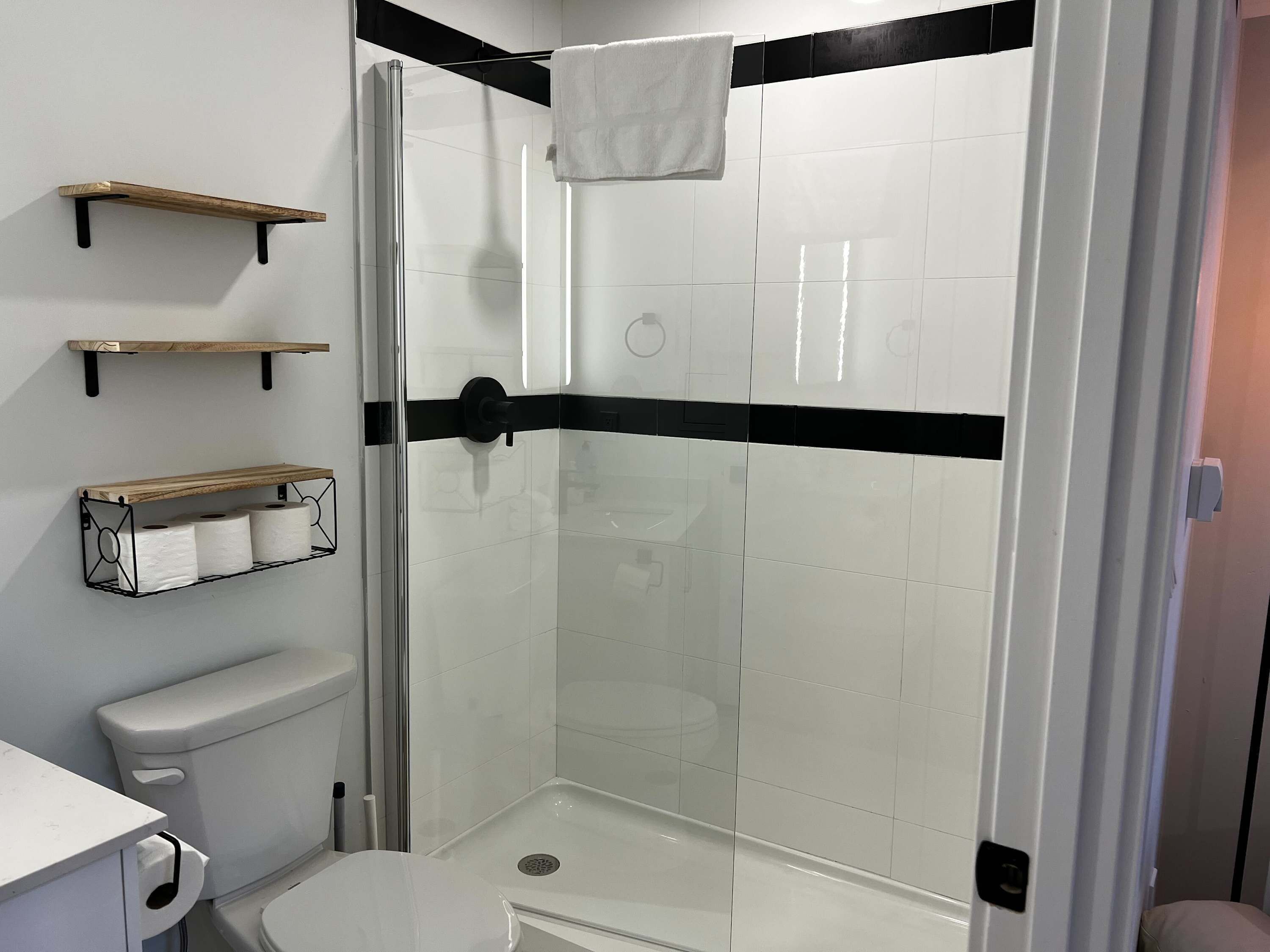 Een moderne badkamer met een douchecabine van glas, witte tegels, zwarte accessoires en houten planken.