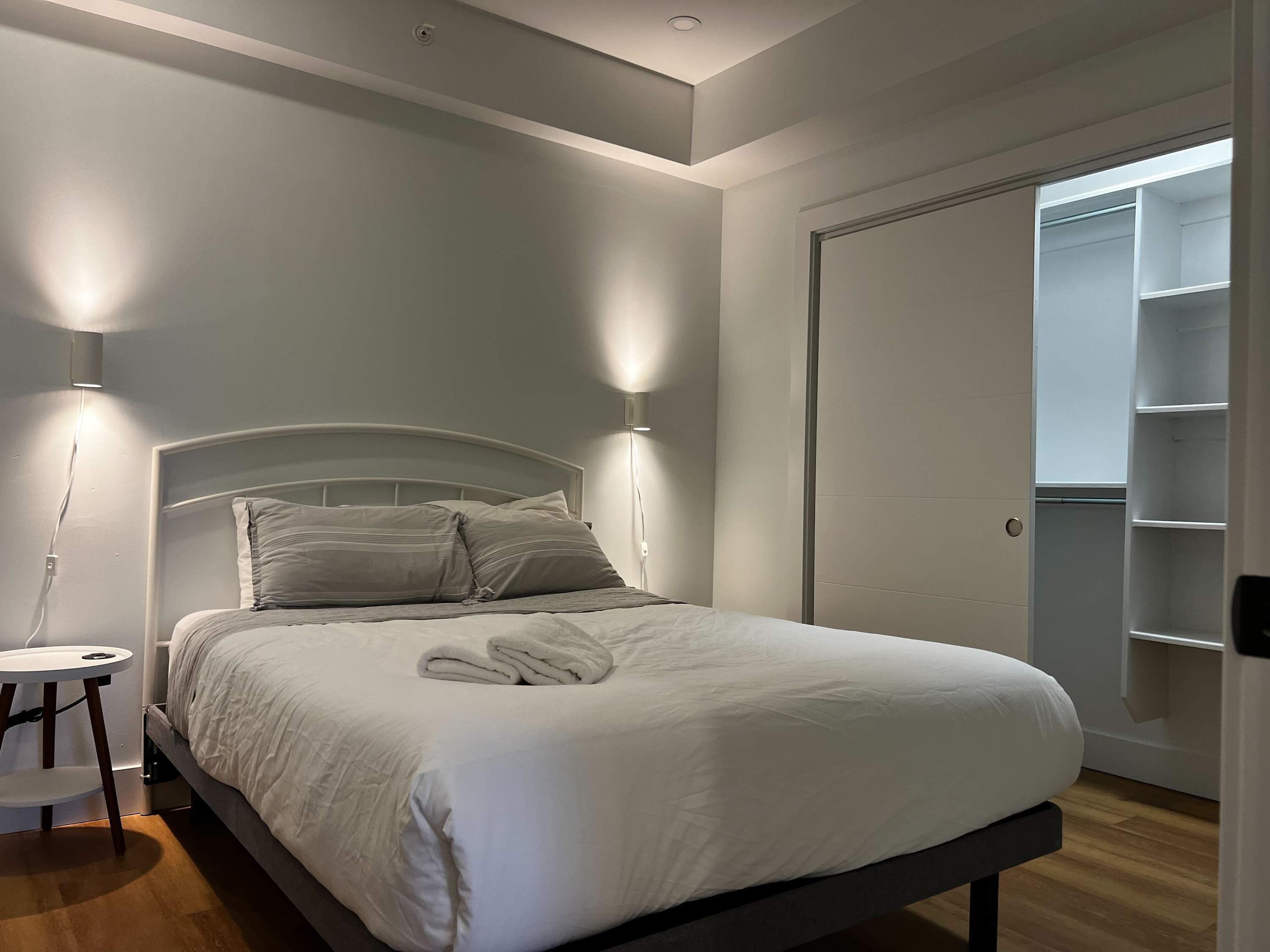 A neatly made bed with white bedding, a bedside table with a lamp, and a closet with shelves.