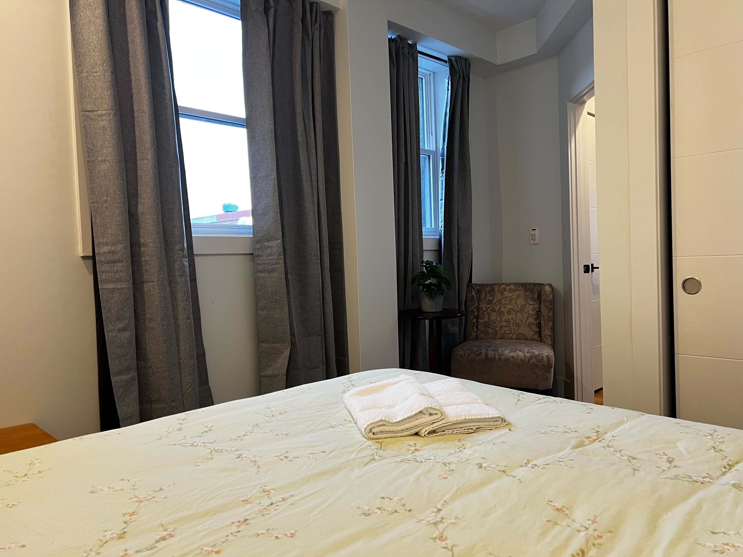 Een slaapkamer met een bed, gordijnen, een stoel en een deur.