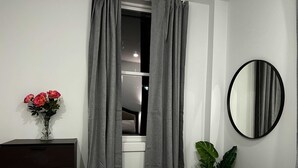 Un dormitorio con cama, cómoda, espejo y ventana con cortinas.