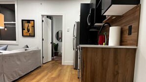 Una cocina moderna con armarios de madera, un cubo de basura de acero inoxidable y un sofá gris en una sala de estar.