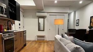 Una cocina moderna con horno empotrado y microondas, un comedor con sofá y mesa, y un pasillo con lámpara y puerta.
