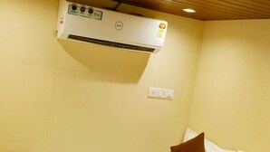 Een enkel bed met wit beddengoed en bruine kussens, een airconditioningunit aan de muur en een stopcontact.
