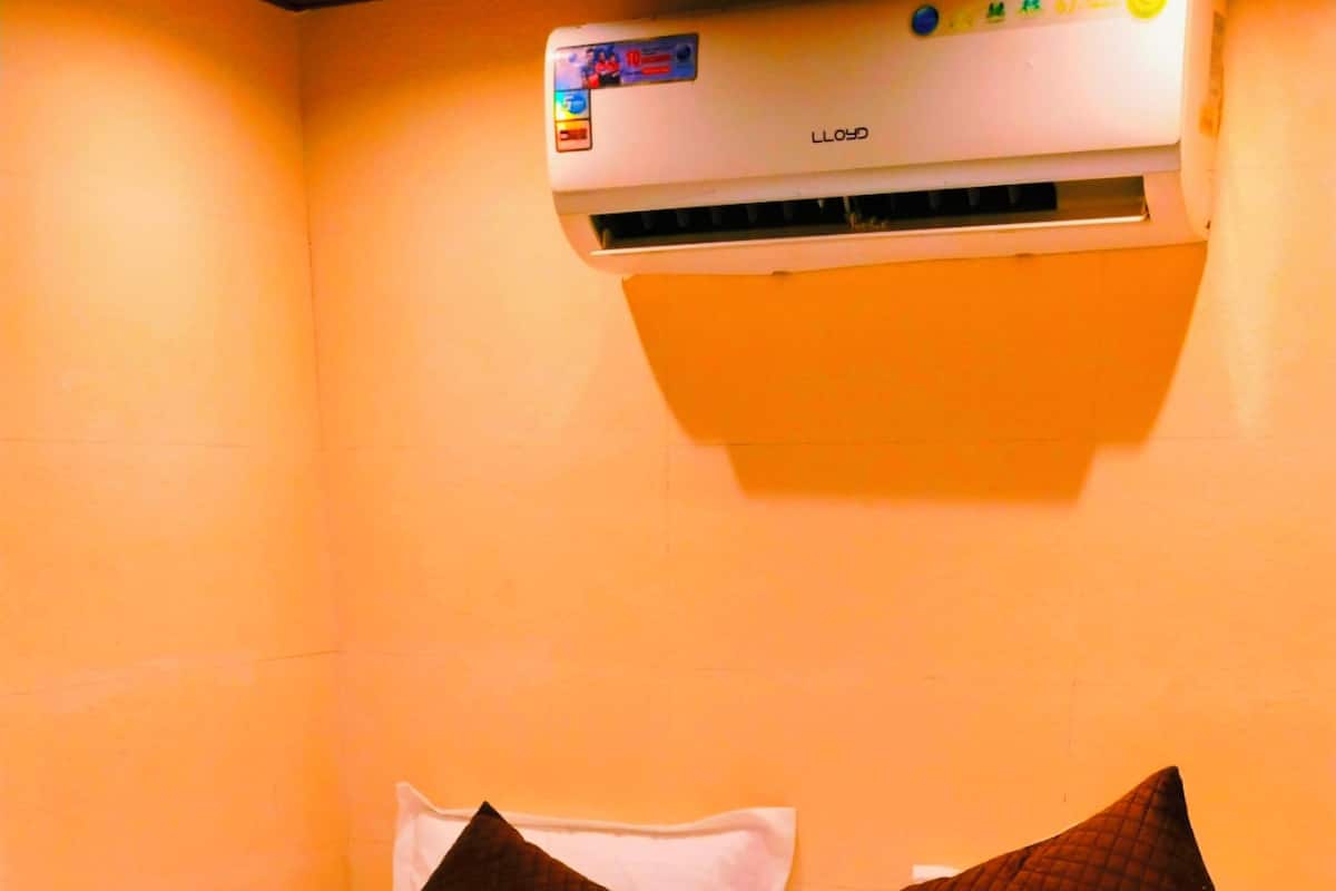 A hotel room with a bed, pillows, and a wall-mounted air conditioner.