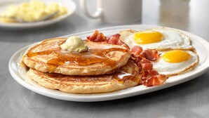 Een ontbijtbord met pannenkoeken, twee gebakken eieren en spek.