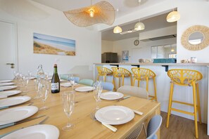 A dining area with a long wooden table set for a meal, yellow chairs, and a bottle of wine.