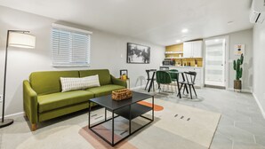 A modern living room with a green sofa, a black coffee table, and a dining area with a green chair and a small table.