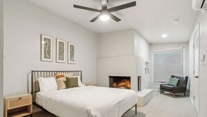 A bedroom with a bed, bedside tables, a fireplace, a chair, and a ceiling fan.