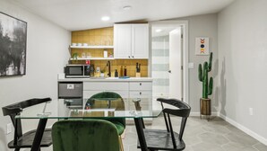 A modern kitchen with white cabinets, a glass dining table, and a green chair.