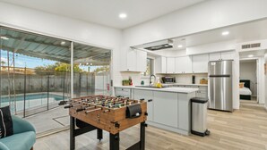 A modern kitchen with a foosball table, a large island, and a view of a swimming pool. - Pool & Games | Peaceful Neighborhood (Phoenix)