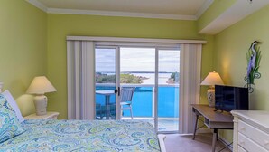 A hotel room with a bed, a desk, a television, a chair, and a view of a body of water. - Sunset Point - 63rd st, 3 BR, Pool (Ocean City)