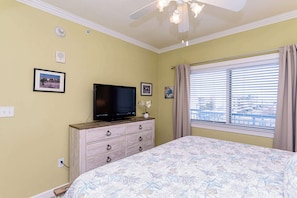 Un dormitorio con cama, cómoda, televisor y ventana con persianas.