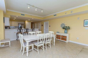A dining area with a white table and chairs, a kitchen in the background, and a clock on the wall. - Sunset Point - 63rd st, 3 BR, Pool (Ocean City)