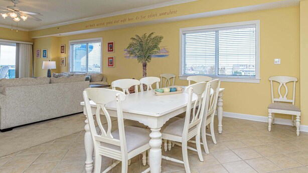 A dining area with a white table and chairs, a vase with a plant, and a view of the outside through the window. - Sunset Point - 63rd st, 3 BR, Pool (Ocean City)