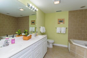 Une salle de bain avec deux lavabos, des toilettes et une baignoire. Des serviettes sont accrochées au mur et un panier contenant des articles de toilette est posé sur le comptoir.