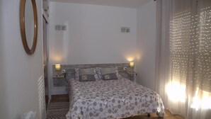 A bedroom with a bed, two bedside lamps, a mirror, and a window with curtains. - CHARMING APARTMENT (Sant Feliu de Guíxols)
