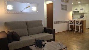 A living room with a sofa, a coffee table, and a kitchen area with a microwave and chairs. - CHARMING APARTMENT (Sant Feliu de Guíxols)