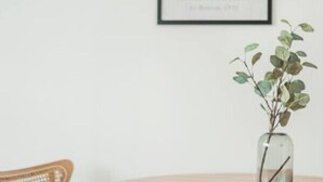 Ein runder Holztisch mit einem Stuhl, ein gerahmtes Kunstwerk an der Wand und eine kleine Vase mit einer Pflanze auf dem Tisch.