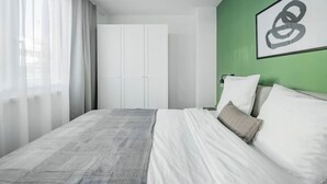 Ein Hotelzimmer mit Bett, weißen Vorhängen, einer grün gestrichenen Wand und einem gerahmten Kunstwerk.