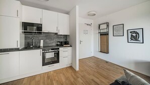 Una cocina moderna con armarios blancos, horno empotrado y microondas. Hay dos cuadros enmarcados en la pared y piso de madera.
