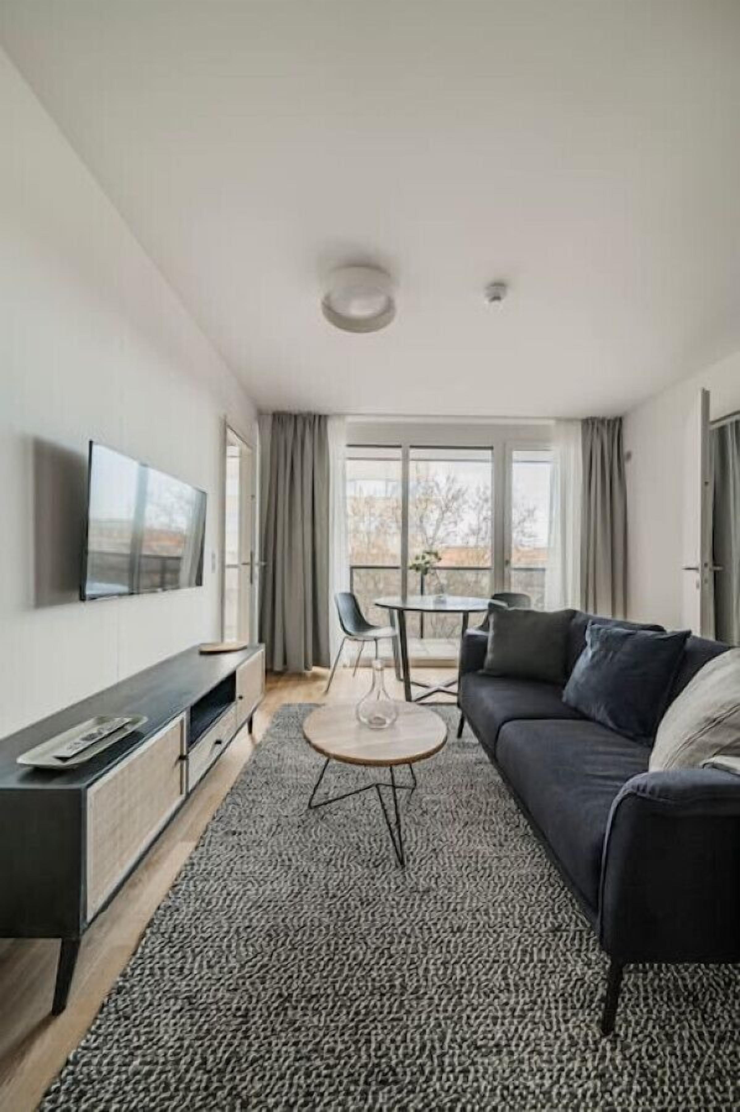 Ein modernes Wohnzimmer mit einer Couch, einem Couchtisch, einem an der Wand befestigten Fernseher und einem Balkon mit Tisch und Stühlen.